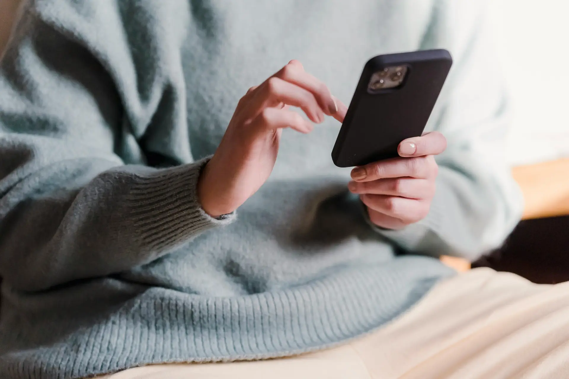 Crop faceless female in casual clothes using smartphone and touching screen while chilling at home